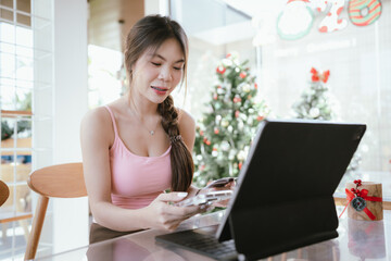 An Asian woman using a smartphone and credit card while shopping online during the Christmas...