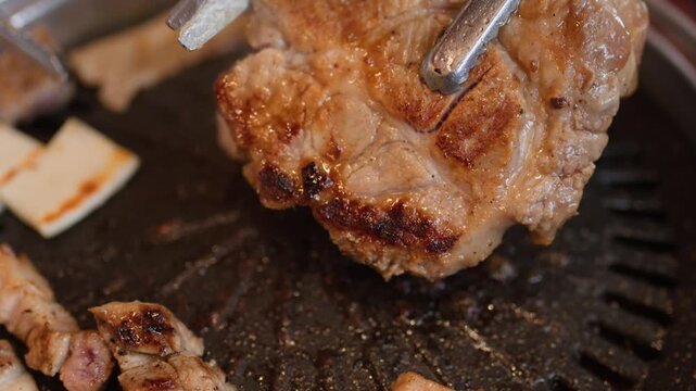 Close Up of Tongs Lifting and Cutting Grilled Meat on Korean BBQ Grill