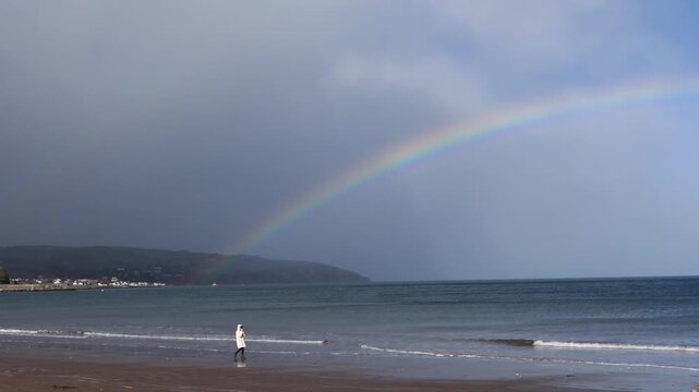 Walkers of the beautiful Glenariff Waterfoot Beach on the Irish Sea Co Antrim Northern Ireland with a Rainbow over sea 12-26-2025
