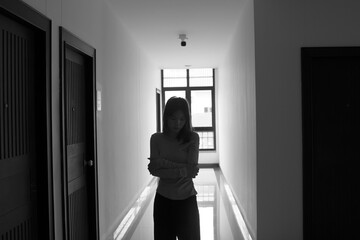 A lonely young woman sits on the floor in a narrow hallway, clutching her head in despair,...