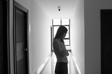 A lonely young woman sits on the floor in a narrow hallway, clutching her head in despair, expressing sadness, stress, and emotional conflict in the quiet, simple interior of the building. The image i