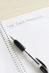 Close up shot of handwriting "New Year's Resolutions" on new notebook with black pen on white wooden table.