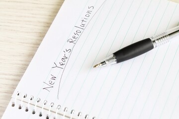 Close up shot of handwriting "New Year's Resolutions" on new notebook with black pen on white wooden table.