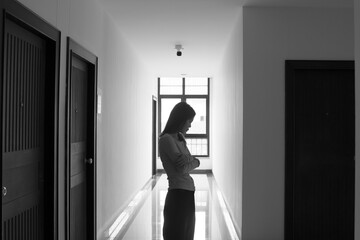 A lonely young woman sits on the floor in a narrow hallway, clutching her head in despair, expressing sadness, stress, and emotional conflict in the quiet, simple interior of the building. The image i