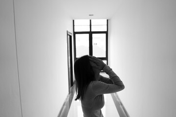 A lonely young woman sits on the floor in a narrow hallway, clutching her head in despair, expressing sadness, stress, and emotional conflict in the quiet, simple interior of the building. The image i