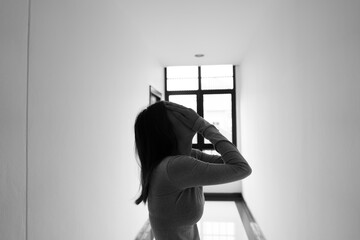 A lonely young woman sits on the floor in a narrow hallway, clutching her head in despair, expressing sadness, stress, and emotional conflict in the quiet, simple interior of the building. The image i