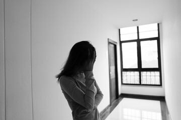 A lonely young woman sits on the floor in a narrow hallway, clutching her head in despair, expressing sadness, stress, and emotional conflict in the quiet, simple interior of the building. The image i