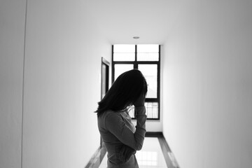 A lonely young woman sits on the floor in a narrow hallway, clutching her head in despair, expressing sadness, stress, and emotional conflict in the quiet, simple interior of the building. The image i