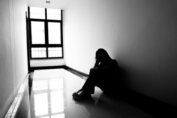 A lonely young woman sits on the floor in a narrow hallway, clutching her head in despair, expressing sadness, stress, and emotional conflict in the quiet, simple interior of the building. The image i