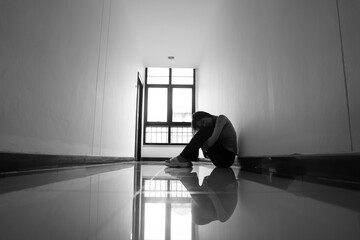 A lonely young woman sits on the floor in a narrow hallway, clutching her head in despair, expressing sadness, stress, and emotional conflict in the quiet, simple interior of the building. The image i