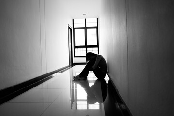 A lonely young woman sits on the floor in a narrow hallway, clutching her head in despair, expressing sadness, stress, and emotional conflict in the quiet, simple interior of the building. The image i