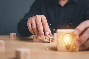 Man arranging wooden cubes with brain symbols and glowing lightbulb for business innovation