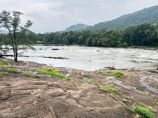 Chalakudy River flowing with rocky banks and lush forested Western Ghats mountains in the background near Athirappilly Falls in Thrissur district, Kerala.