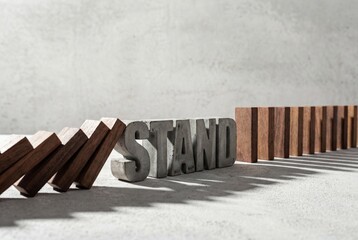 Concrete word stand stops falling wooden dominoes showing resilience and strength against crisis