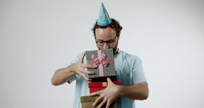 A cheerful man with glasses and a birthday hat carefully holds a stack of colorful gift boxes. He smiles with anticipation and excitement. Perfect for birthday celebrations, surprises, and gift-giving