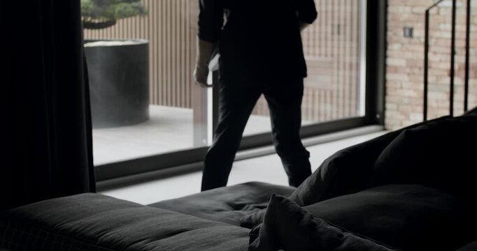 A man is sitting on the black sofa and reading a book. Modern contemporary Minimalist living room with bricks wall, large sliding windows and black furniture. Cozy Modern Furniture Design.