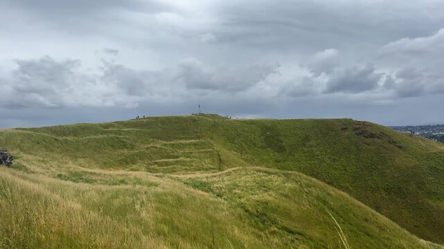 A panoramic view of a green dormant volcano crater and grass field under blue semi-cloudy sky.