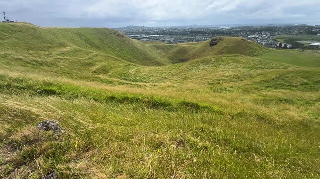 A panoramic view of a green dormant volcano crater and grass field under blue semi-cloudy sky.