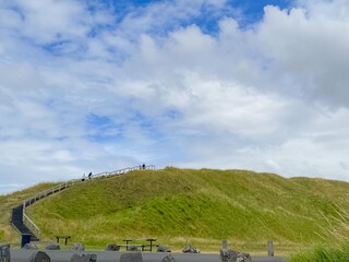 A panoramic view of a green dormant volcano crater and grass field under blue semi-cloudy sky.