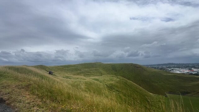 A panoramic view of a green dormant volcano crater and grass field under blue semi-cloudy sky.