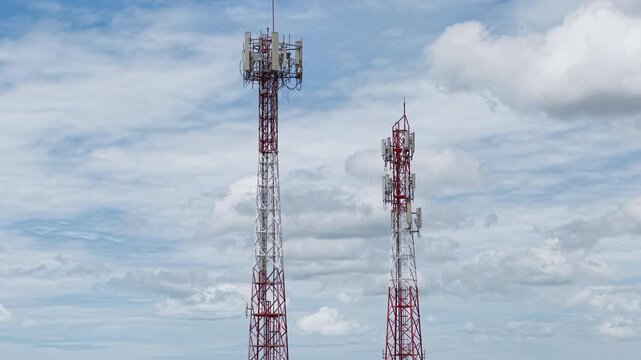 Pedestal Shot of Two Telecommunication Towers Against a Blue Sky with White Clouds