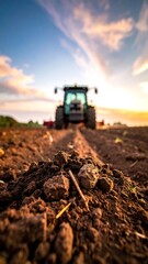 Farm field with tractor at golden hour. Soil focus, sky clouds in background, soft natural light, earthy tones
