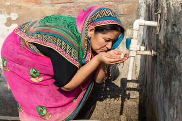 Thirsty rural Indian woman drinking fresh clean water from a tap outdoor, People of India. Scarcity. © GAJENDRRA BHATI 