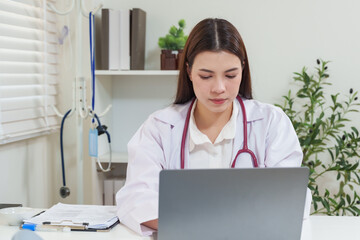Asian female physician using laptop at clinic desk for reviewing electronic health records, analyzing patient data and making notes, modern medical technology used for digital healthcare management