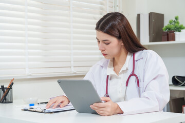 Asian female doctor holding tablet reviewing medical information during telemedicine consultation providing online healthcare service and remote diagnosis through digital telehealth technology