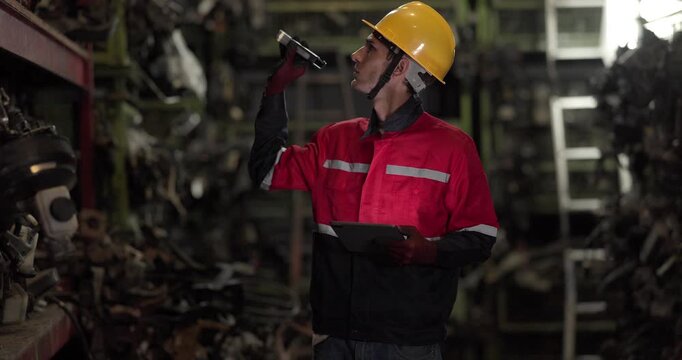 A warehouse technician uses a flashlight and tablet to examine used automotive parts on dim shelves, conducting quality and inventory checks.
