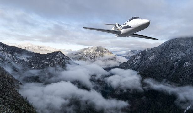 Private Jet Soaring Over Snowy Mountain Range Above Cloudy Valley in British Columbia