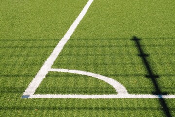 Corner of a soccer field with white lines and shadow of goalpost, green grass background