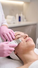 Ultrasonic skin scrubber facial treatment with pink gloves close up
