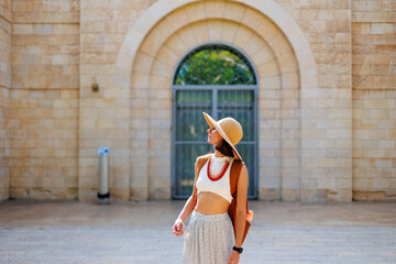 A stylish fashionable girl traveler in a brown hat with a backpack stands in front of an old house while traveling. visiting a museum while traveling. © zhukovvvlad