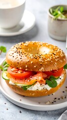 Toasted sesame bagel with lox, cream cheese, tomato, cucumber, and greens, sits on a white plate, gray background