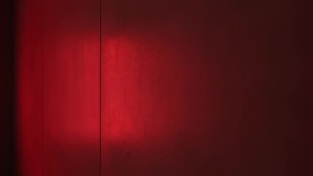 Static shot of a sleek minimalist wall texture where the rich ruby red ambient light slowly increases intensity creating a deep, evolving atmospheric glow slowly, concept, darkness