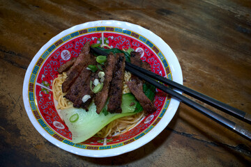 A bowl of ramen noodle and sliced cow meats, Japanese food with black chopsticks on a wooden table