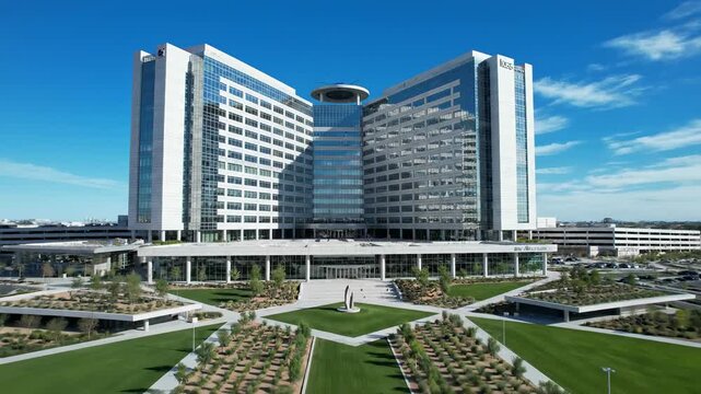 Static wide establishing shot slowly zooming out from the vast modern hospital structure surrounded by clear sky and minimal contemporary landscaping healthcare, minimal, contemporary