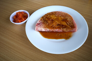 Fresh raw beef on a white plate ready to be grilled, on a wooden table