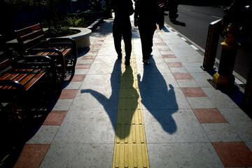 Yellow tactile paving for blind people or visually impaired and human shadow on the sidewalk