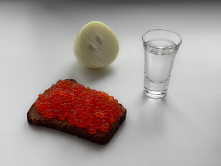 A still life, a glass of vodka, a sandwich with red caviar and an onion.
