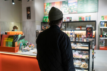 A person stands at the counter in a food shop looking at the display case filled with items