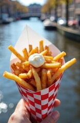 Crispy fried potatoes served in red checkered paper cone with mayonnaise topping. Enjoy this tasty dutch street food snack alongside amsterdam canal.