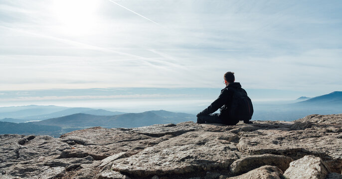 Man sitting on rocky mountain enjoying panoramic view at sunrise