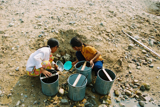 Rural children digging for water in dry riverbed during drought conditions, film photography.