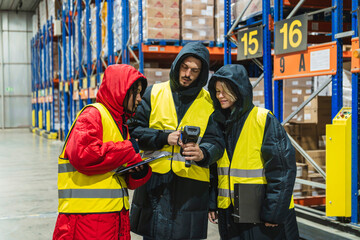 Group of diverse workers managing inventory with barcode scanner and clipboard in a low temperature...