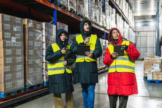 Group of diverse workers wearing protective cold weather gear and high visibility vests checking inventory in a refrigerated logistics warehouse - Powered by Adobe