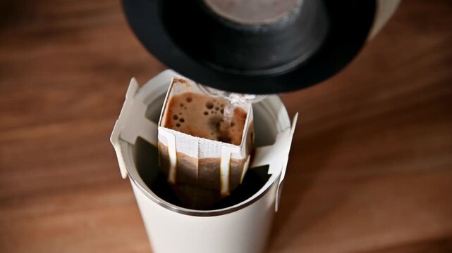 Preparing a fragrant drink from natural ground coffee in a drip bag at home. Boiling water is poured into the drip bag and filter. Close-up.
