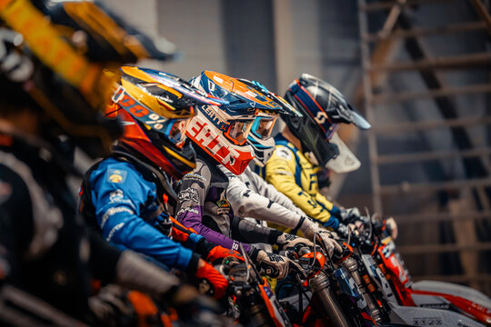 Latvia, Riga, 2025-08-27, regular training. Motocross riders in colorful gear preparing for a race on their dirt bikes at an indoor track