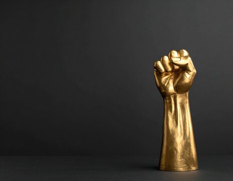 Golden fist statue symbolizing power, strength, and solidarity. Minimalist banner with raised gold fist symbol as abstract sculpture on dark background. For Juneteenth, Black Histry Month. 